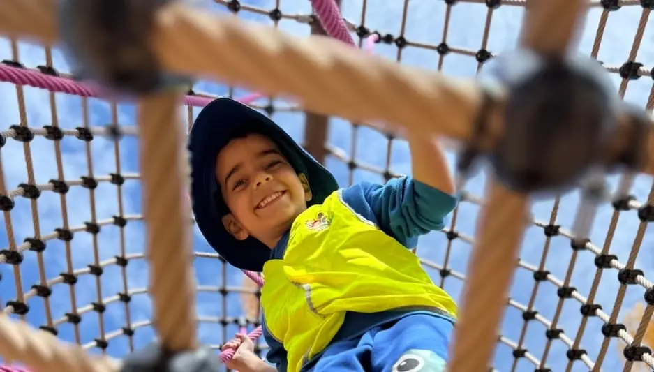 A child smiling while climbing through an outdoor play structure at Kids Kingdom.
