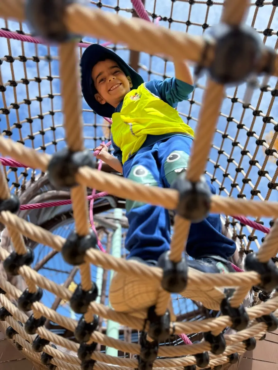 A child climbing a rope obstacle and smiling during active outdoor play.