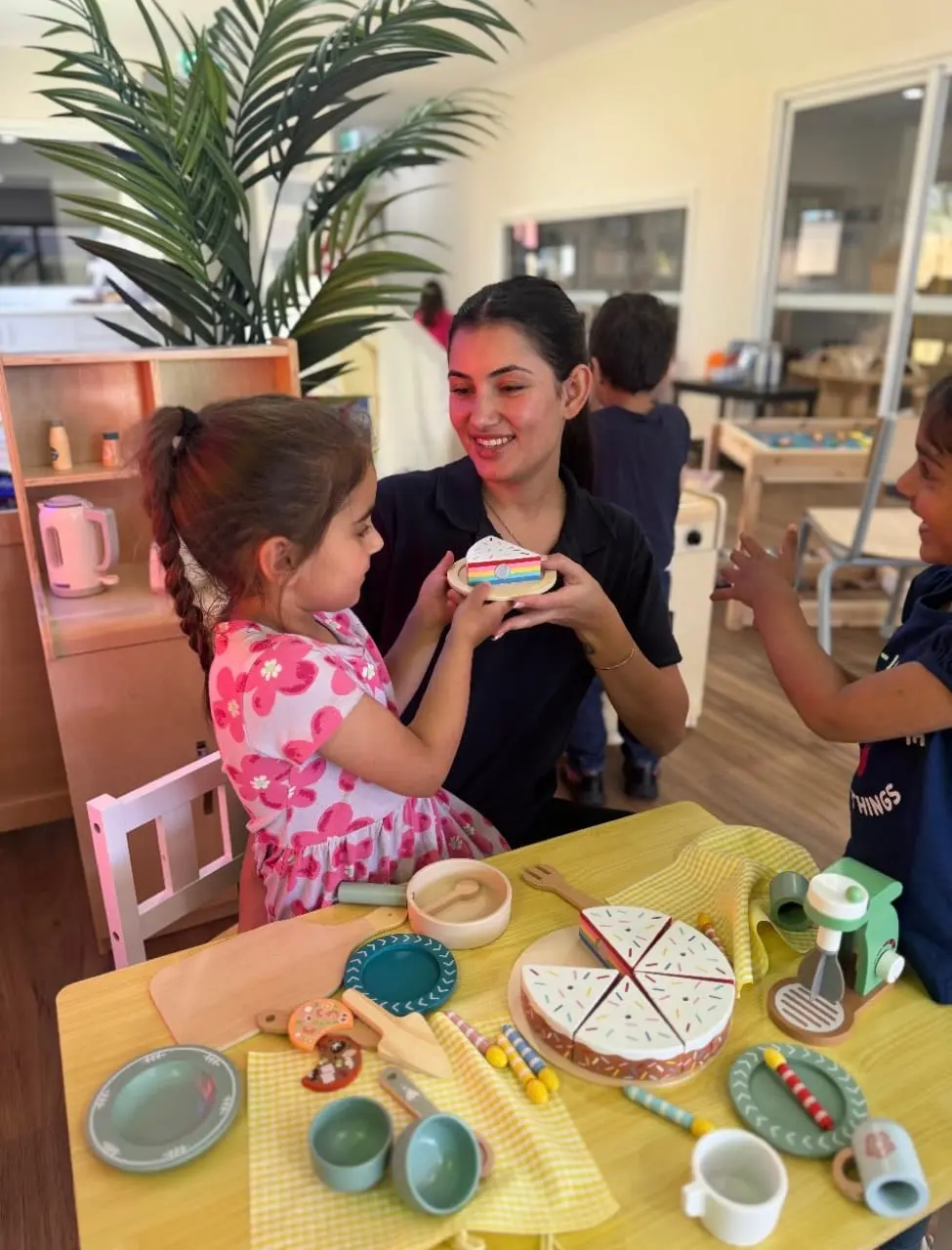 Children and an educator sharing a tea-party dramatic play experience indoors.